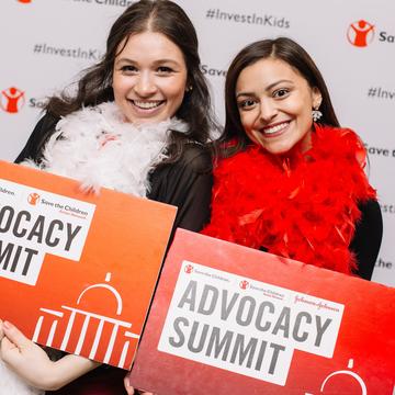 Two Save the Children staff members hold red signs that read, Advocacy Summit: while standing in front of a white mural with Save the Children’s logo and the hashtag #InvestinKids printed on it. Photo credit: Rachel Couch/ Save the Children, March 2019. Two Save the Children staff members hold red signs that read, Advocacy Summit: while standing in front of a white mural with Save the Children’s logo and the hashtag #InvestinKids printed on it. Photo credit: Rachel Couch/ Save the Children, March 2019.