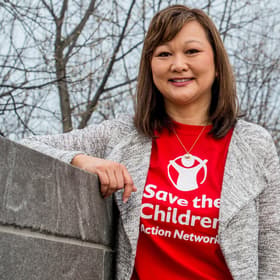 A woman wearing a red Save the Children Action Network t-shirt and stands in front of the Capitol Building in Washington D.C. Photo credit: Susan Warner/Save the Children, March 2017. A woman wearing a red Save the Children Action Network t-shirt and stands in front of the Capitol Building in Washington D.C. Photo credit: Susan Warner/Save the Children, March 2017.