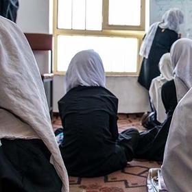 In Afghanistan, a female teachers stands in front of a room filled with girls and boys. In Afghanistan, a female teachers stands in front of a room filled with girls and boys.