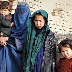 In Afghanistan, a mother holds her baby while standing next to three of her daughters in front of a crumbling brick wall. In Afghanistan, a mother holds her baby while standing next to three of her daughters in front of a crumbling brick wall.