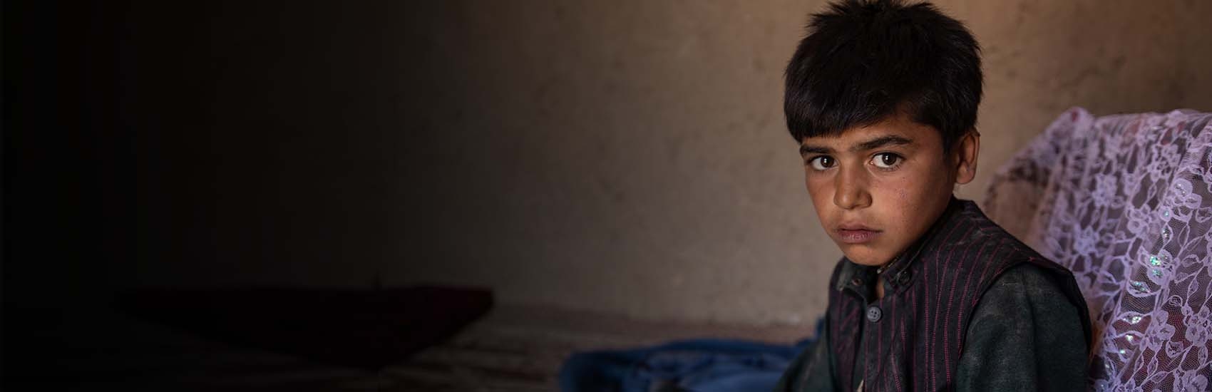 A young afghan boy sits in a shelter. 