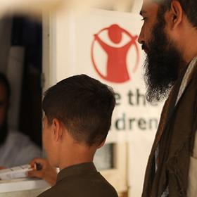 A young boy with his back to the camera stands with an adult man in front of a pharmacy window in Afghanistan A young boy with his back to the camera stands with an adult man in front of a pharmacy window in Afghanistan