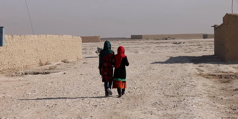 Two girls walk down a dirt road in Afghanistan. Two girls walk down a dirt road in Afghanistan.
