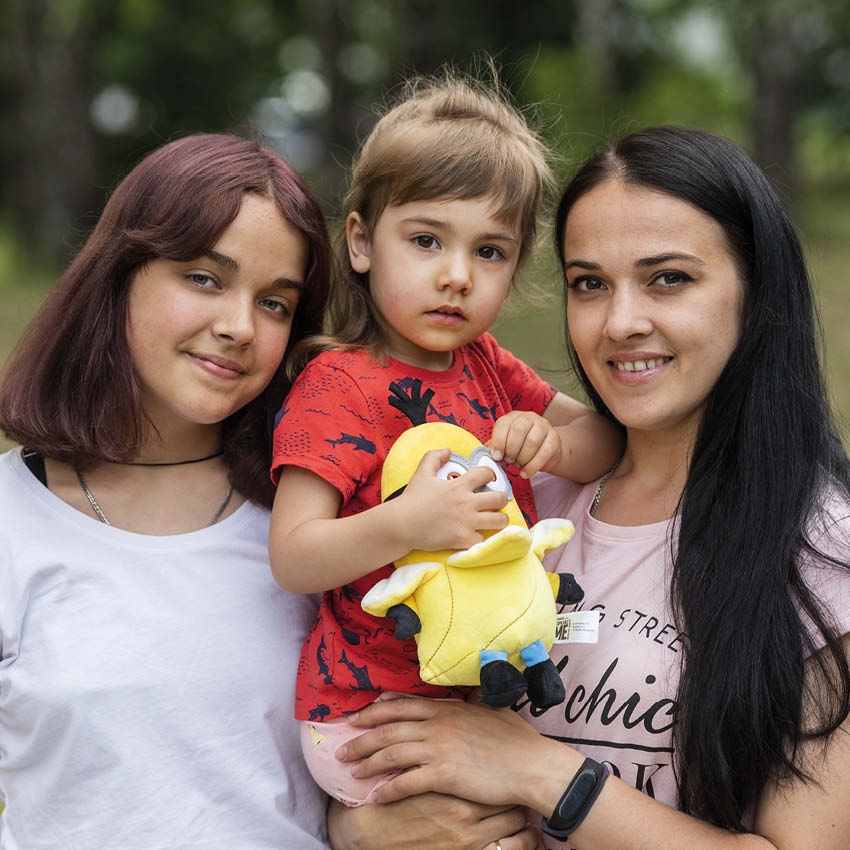 In Romania, a mother stands with her two girls as they smile at the camera. In Romania, a mother stands with her two girls as they smile at the camera.
