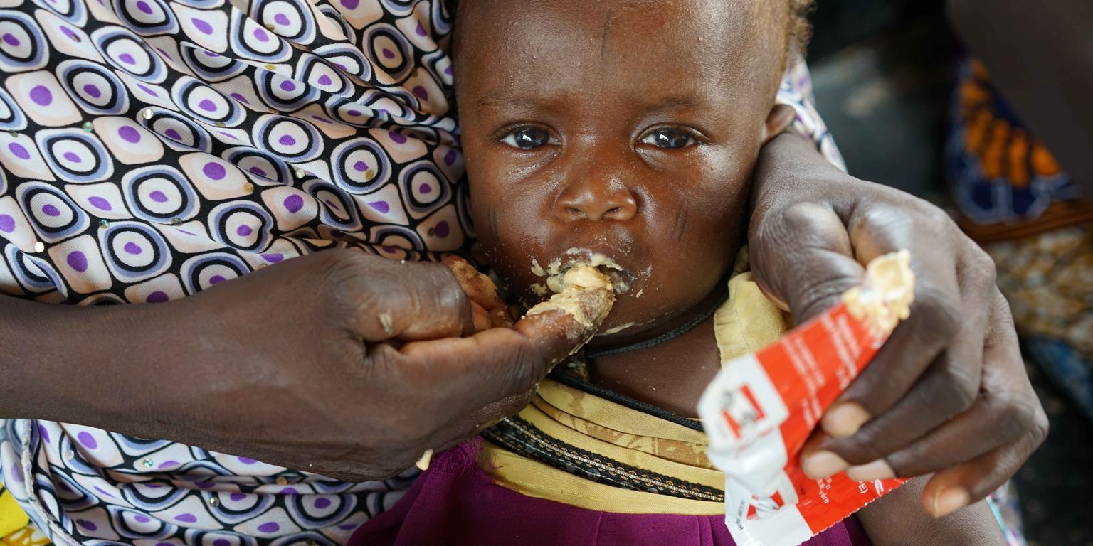 An infant of 9 months, with her mother Alima, eats high nutrient peanut paste as a distribution at the Guidanaoutchi Clinic, Niger. Photo Credit Save the Children 2016. An infant of 9 months, with her mother Alima, eats high nutrient peanut paste as a distribution at the Guidanaoutchi Clinic, Niger. Photo Credit Save the Children 2016.
