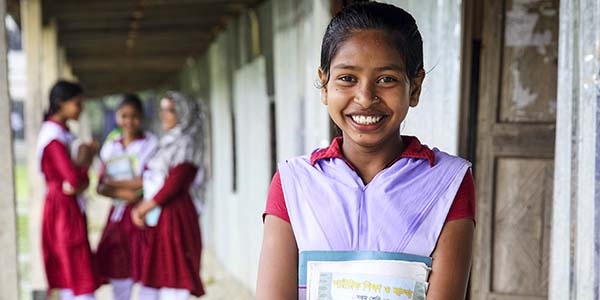 A teenage girl smiles at the camera. Three girls are out of focus standing behind her. A teenage girl smiles at the camera. Three girls are out of focus standing behind her.