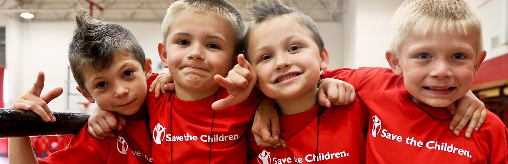 Four boys in red Save the Children t-shirts smile at the camera