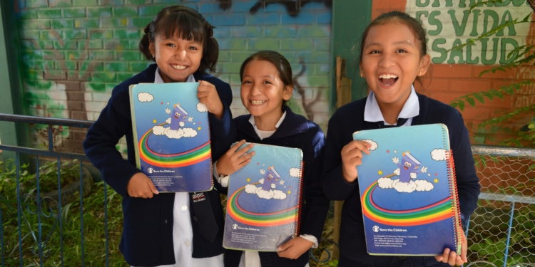 A group of three girls wearing school uniforms hold books outside a school in Bolivia. A group of three girls wearing school uniforms hold books outside a school in Bolivia.
