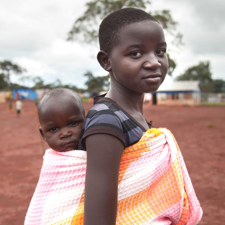 A young girl in Burundi carries a small child on her back using a cloth sling. A young girl in Burundi carries a small child on her back using a cloth sling.