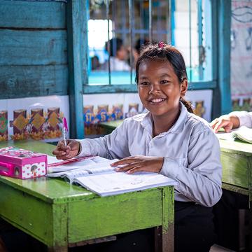 In Cambodia, a young girl sits at a desk reading. In Cambodia, a young girl sits at a desk reading.