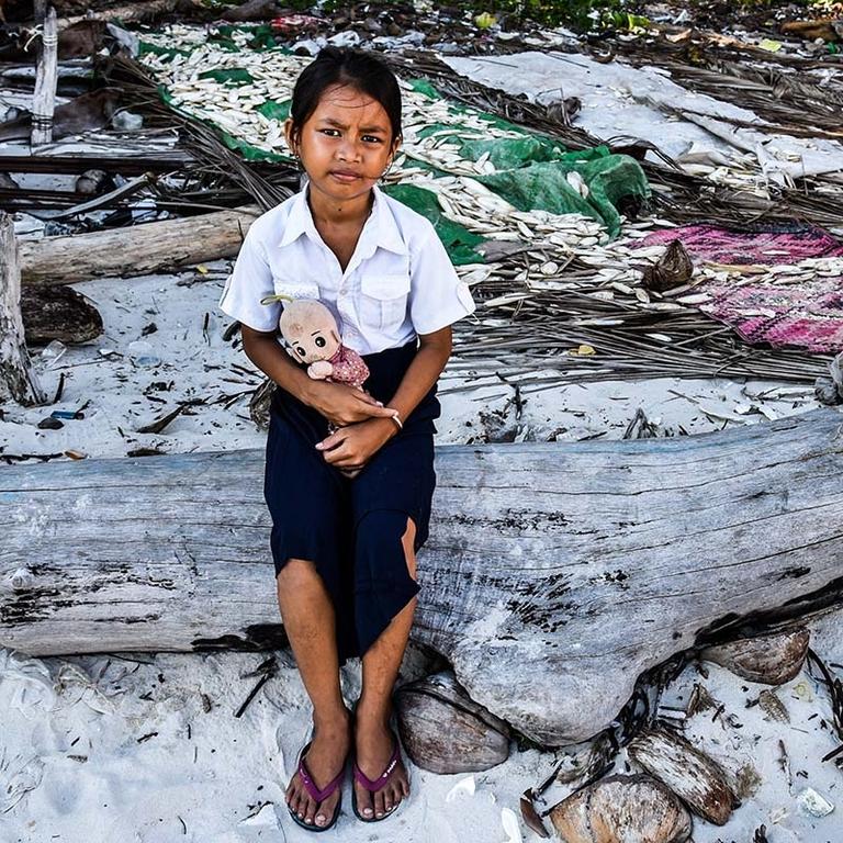 In Cambodia, a girl holds a stuffed animal while leaning against a piece of wood against the backdrop of storm-damaged homes. In Cambodia, a girl holds a stuffed animal while leaning against a piece of wood against the backdrop of storm-damaged homes.