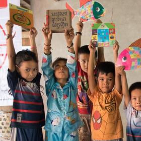Children stand with their hands above their heads, happily holding favorite books and drawings. Children stand with their hands above their heads, happily holding favorite books and drawings.