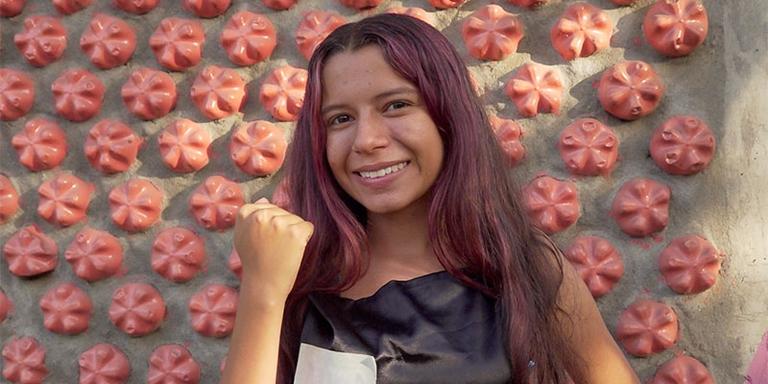 A strong girl in Columbia stands in front of the house she helped build out of water bottles A strong girl in Columbia stands in front of the house she helped build out of water bottles