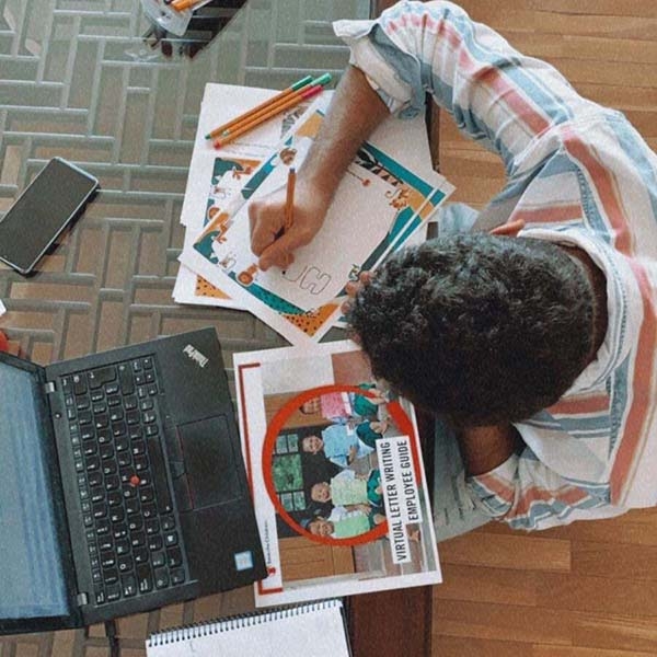 Overhead shot of a child at a laptop writing on a piece of paper. Overhead shot of a child at a laptop writing on a piece of paper.