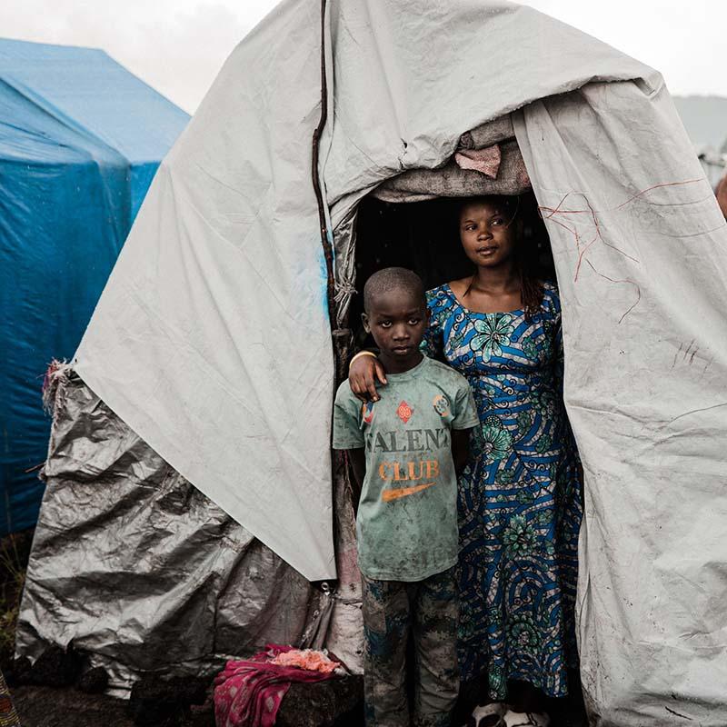 A mother stands with her son in a tent in the DRC.
