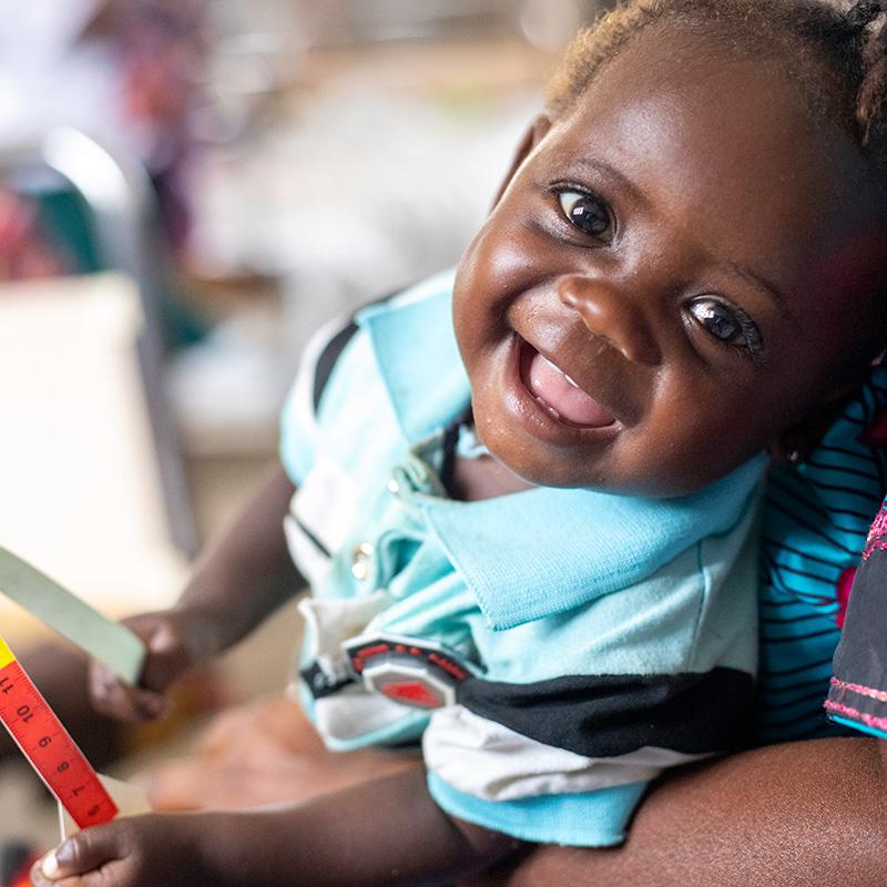 In DRC, a baby girl in a light blue shirt sits on her mother's lap smiling at the camera