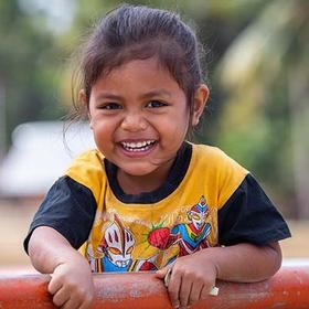 in Indonesia, a young girl smiles while leaning on an outdoor structure. in Indonesia, a young girl smiles while leaning on an outdoor structure.