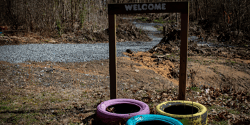 Three large tired with chipped paint sit under a Welcome sign in a wooded area in West Virginia. Three large tired with chipped paint sit under a Welcome sign in a wooded area in West Virginia.