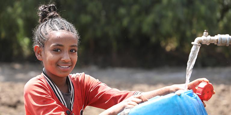 A girl in Ethiopia in an orange shirt fills a jug of water from a tap A girl in Ethiopia in an orange shirt fills a jug of water from a tap