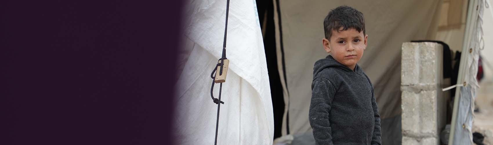 A young boy from Lebanon stands outside a tent in a displacement camp in Syria for refugees who have had to flee conflict.