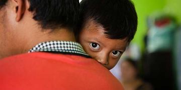 3-year-old Esbin peeks at us over his father’s shoulder in an emergency shelter. 3-year-old Esbin peeks at us over his father’s shoulder in an emergency shelter.