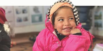 A little girl in a pink jacket looks away from the camera and smiles A little girl in a pink jacket looks away from the camera and smiles