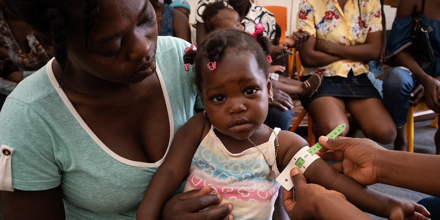 Haiti, a mother holds her small daughter who's arm is being measured for malnutrition Haiti, a mother holds her small daughter who's arm is being measured for malnutrition