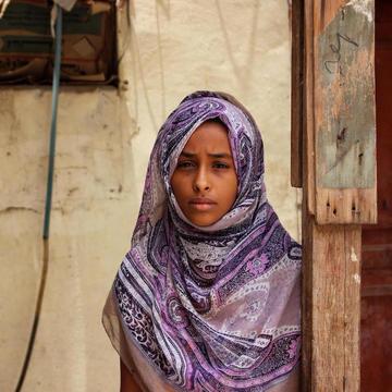 A girl stands in front of a wall marked with bullet holes in Yemen. A girl stands in front of a wall marked with bullet holes in Yemen.