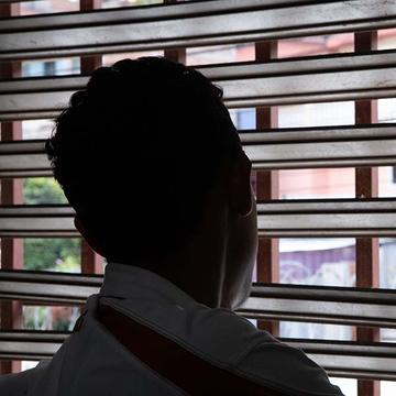 Standing in the shadows so his identify is hidden, 17-year-old Hector looks out the window of his home, in between the openings in the blinds. Standing in the shadows so his identify is hidden, 17-year-old Hector looks out the window of his home, in between the openings in the blinds.