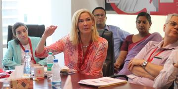 Adults attending a meeting together wear red Save the Children lanyards around their necks and listen intently to a woman speaking. Photo credit: Save the Children 2018. Adults attending a meeting together wear red Save the Children lanyards around their necks and listen intently to a woman speaking. Photo credit: Save the Children 2018.