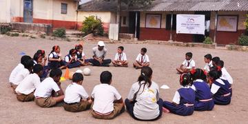 A group of children sit on the ground in a circle at a school in Induri, Maharashtra, India. Their attention is on a teacher. These play sessions are sponsored by Mondelez, and involve learning nutrition and playing games to reinforce a positive message about exercise and good nutrition. Photo credit: Luciana Bonifacio / Save the Children, November 2015. A group of children sit on the ground in a circle at a school in Induri, Maharashtra, India. Their attention is on a teacher. These play sessions are sponsored by Mondelez, and involve learning nutrition and playing games to reinforce a positive message about exercise and good nutrition. Photo credit: Luciana Bonifacio / Save the Children, November 2015.