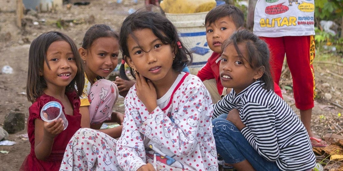 A group of seven young children are gathered in a space littered with branches, blankets and trash. When their homes were destroyed in the 2018 Indonesia earthquake and tsunami, theylived in a temporary shelter and survived on supplies provided by Save the Children and other aid organizations. Photo credit: Ardiles Rante / Save the Children, Oct 2018.