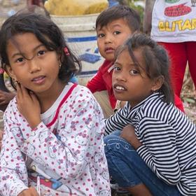 A group of seven young children are gathered in a space littered with branches, blankets and trash. When their homes were destroyed in the 2018 Indonesia earthquake and tsunami, theylived in a temporary shelter and survived on supplies provided by Save the Children and other aid organizations. Photo credit: Ardiles Rante / Save the Children, Oct 2018. A group of seven young children are gathered in a space littered with branches, blankets and trash. When their homes were destroyed in the 2018 Indonesia earthquake and tsunami, theylived in a temporary shelter and survived on supplies provided by Save the Children and other aid organizations. Photo credit: Ardiles Rante / Save the Children, Oct 2018.