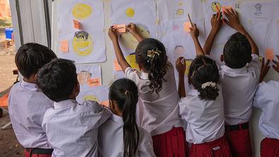 Children sticking notes to a board in a temporary learning space in Indonesia Children sticking notes to a board in a temporary learning space in Indonesia