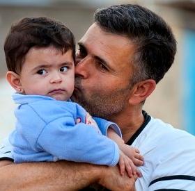 A fourteen month-old boy get a kiss from his father at a refugee camp. Hundreds of thousands of refugees and internally displaced families have fled the violence across Iraq and Syria. Children in Iraq have often witnessed or experienced violence, and left their homes in terrifying circumstances. Many now face hot summers and freezing winters living in tents, half built apartment blocks and public buildings. Save the Children is providing essential goods to families, such as water and hygiene kits, as well A fourteen month-old boy get a kiss from his father at a refugee camp. Hundreds of thousands of refugees and internally displaced families have fled the violence across Iraq and Syria. Children in Iraq have often witnessed or experienced violence, and left their homes in terrifying circumstances. Many now face hot summers and freezing winters living in tents, half built apartment blocks and public buildings. Save the Children is providing essential goods to families, such as water and hygiene kits, as well