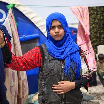 Fourteen-year-old Sulaima stands outside her family’s refugee tent, wearing a blue head scarf and red, flowered shirt – her arm in a cast, with pins. Fourteen-year-old Sulaima stands outside her family’s refugee tent, wearing a blue head scarf and red, flowered shirt – her arm in a cast, with pins.