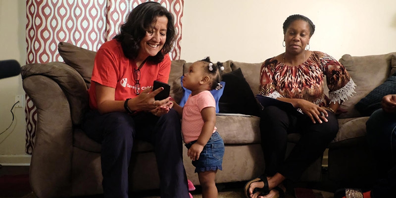 Save the Children CEO Janti Soeripto sits with a child and points to something on her phone. 