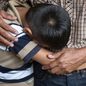 A 12-year old boy buries his face against his father as he mourns the death of his brother in El Salvador. A 12-year old boy buries his face against his father as he mourns the death of his brother in El Salvador.