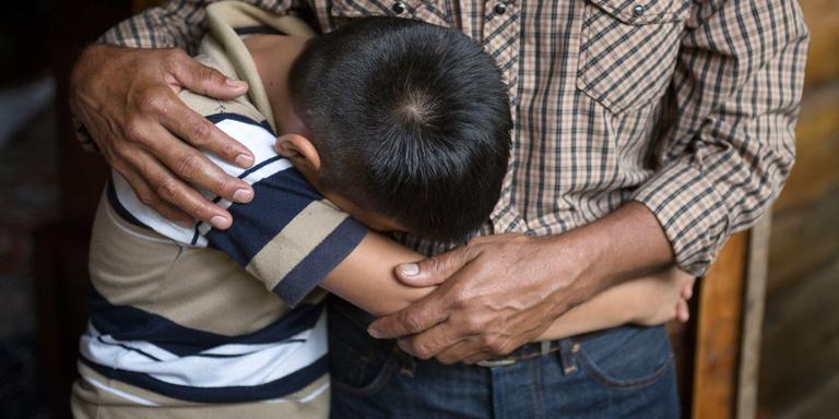A 12-year old boy buries his face against his father as he mourns the death of his brother in El Salvador. A 12-year old boy buries his face against his father as he mourns the death of his brother in El Salvador.