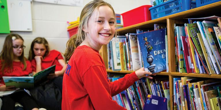 A smiling 10-year-old girl picks a book off a shelf at an in-school literacy program, in Whitley County, Kentucky. Photo credit: Victoria Zegler/Save the Children, December 2017. A smiling 10-year-old girl picks a book off a shelf at an in-school literacy program, in Whitley County, Kentucky. Photo credit: Victoria Zegler/Save the Children, December 2017.