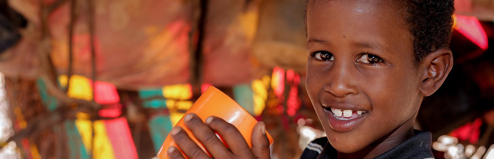 A young boy holds up an orange cup that he saved from flooding at his home in Kenya.