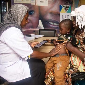 A healthworker holds a a table while conducting an assessment with a child sitting on his mother's lap. A healthworker holds a a table while conducting an assessment with a child sitting on his mother's lap.