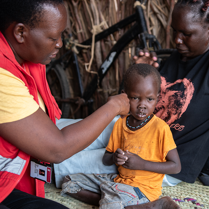A boy in an orange shirt is examined by a healthworker