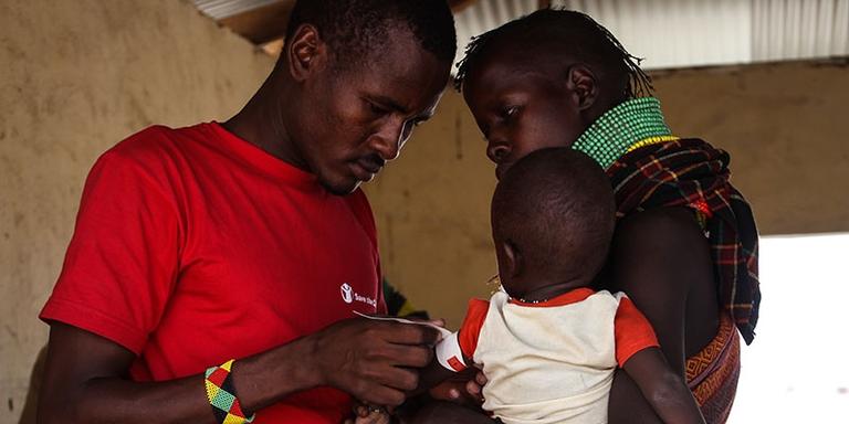 A Save the Children staff member attaches a MUAC band to a small child, who is being held by their mother. A Save the Children staff member attaches a MUAC band to a small child, who is being held by their mother.