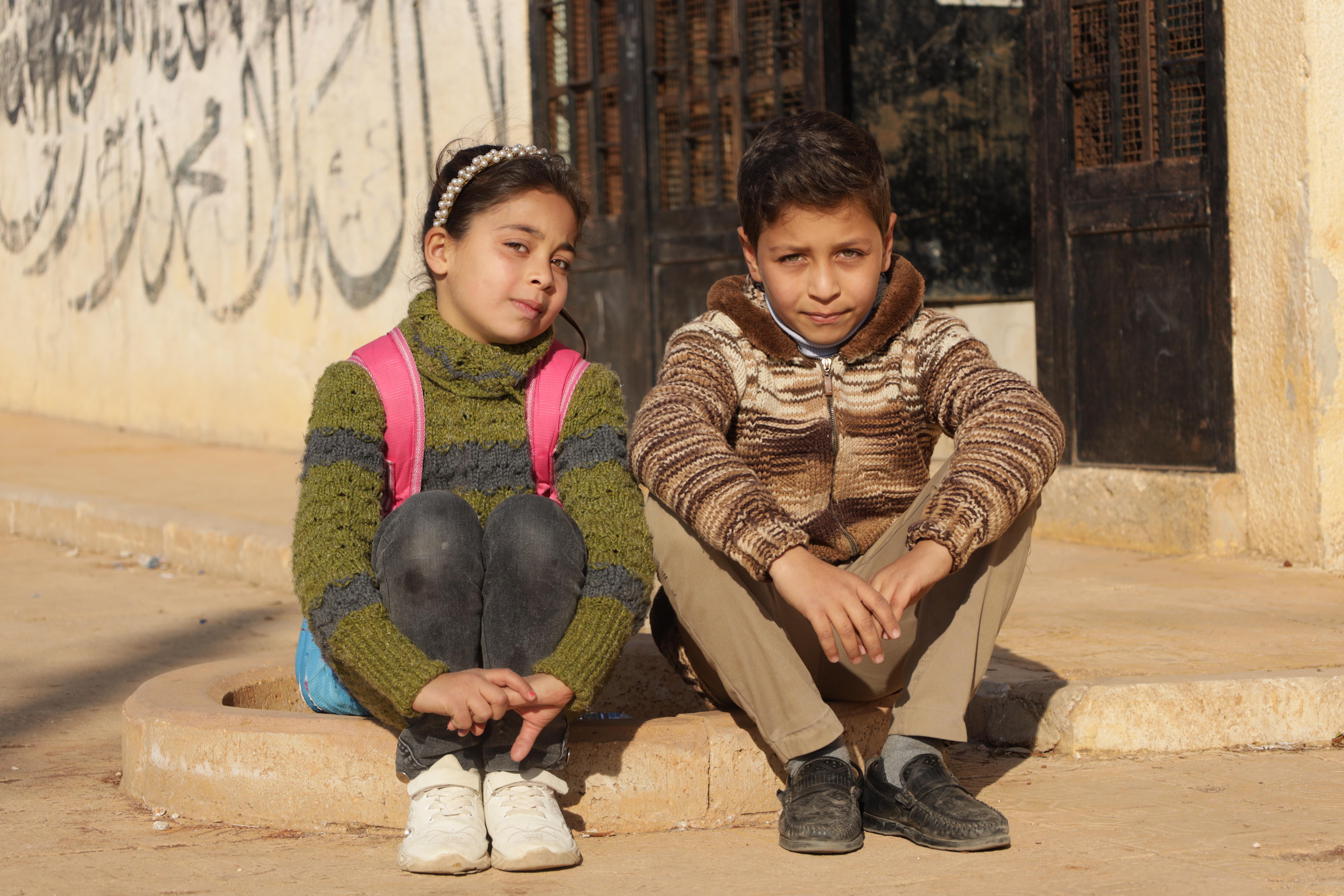 Lana*, 10, & Naji*, 11, sit on the steps outside school, Syria