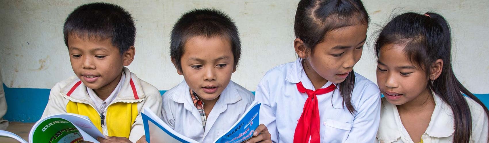 4 children from Laos sit on a step reading books together. 