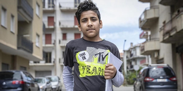A boy stands in the middle of a street holding books. A boy stands in the middle of a street holding books.