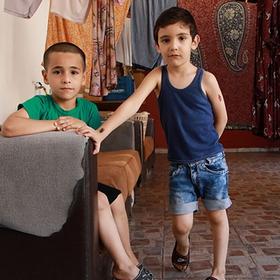 Two boys pose in an empty room. One sits on a couch, the other leans against it. Two boys pose in an empty room. One sits on a couch, the other leans against it.