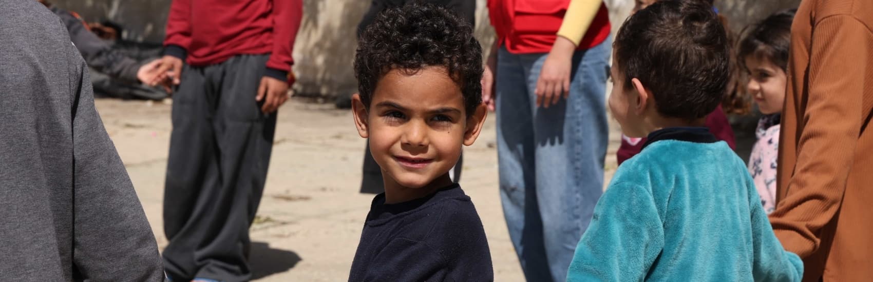Little boy holds hands with other children at child friendly space in Lebanon