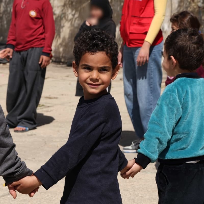 Little boy holds hands with other children at child friendly space in Lebanon